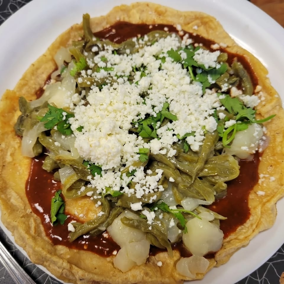 A Mexican huarache topped with red sauce, nopales, onions, cilantro, and crumbled white cheese.