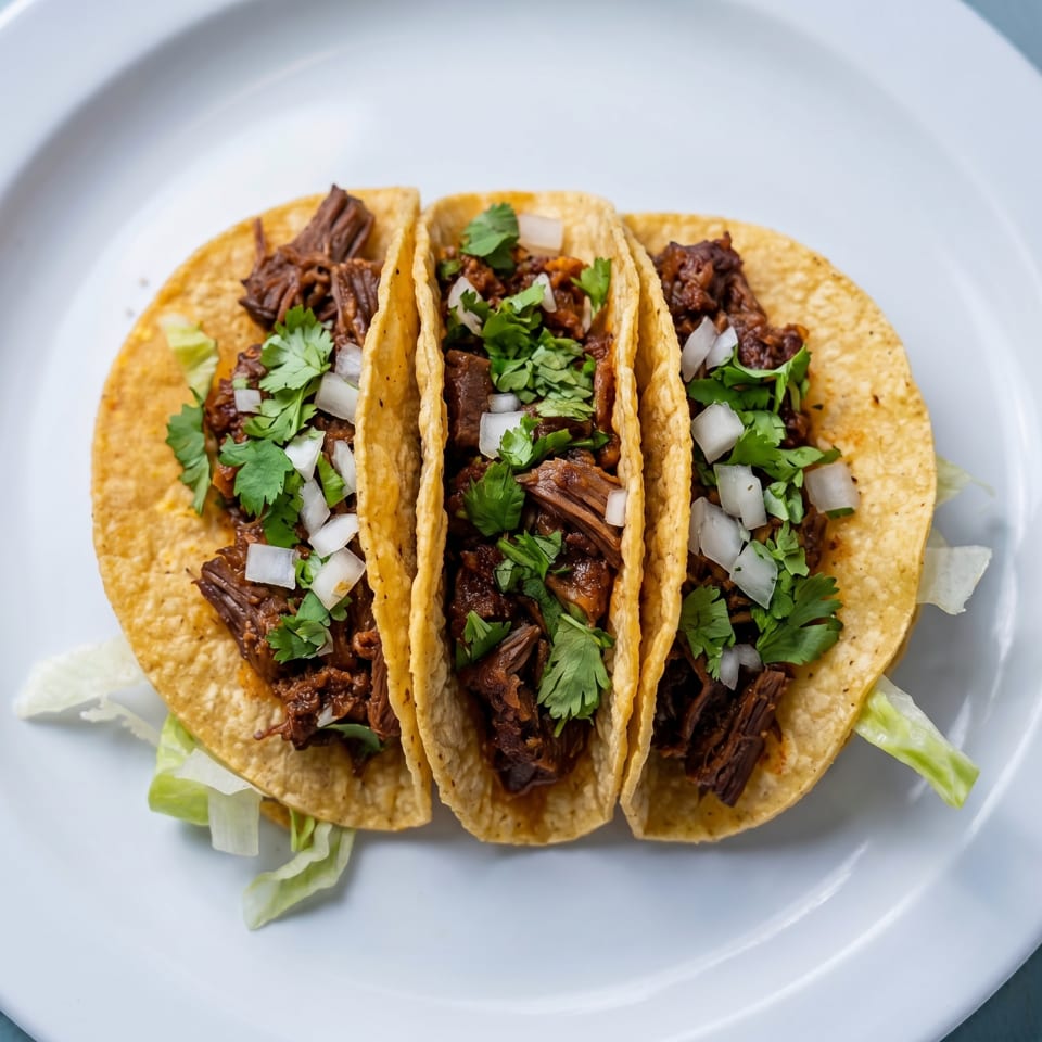 Three beef tacos with cilantro and diced onions on a white plate.